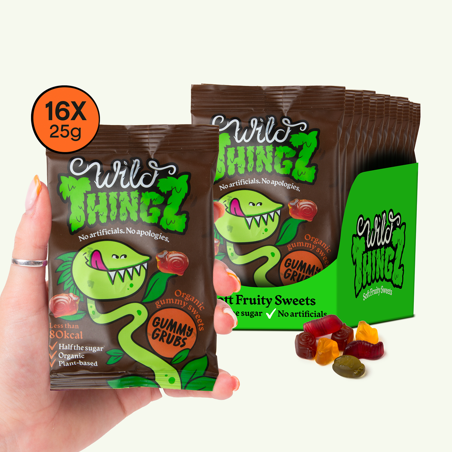 Hand holding a 25g bag of Wild Thingz Organic Gummy Grubs in front of a case of 16 bags