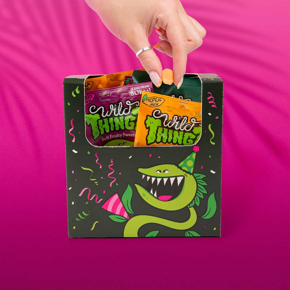 Hand picking a gummy from the open Party Box display on a pink background