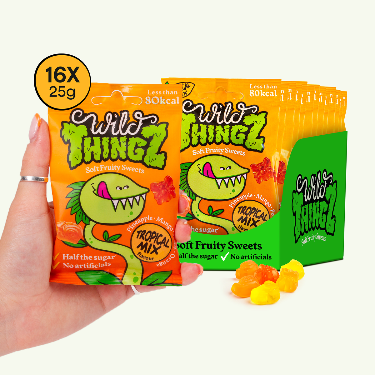 Hand holding a 25g bag of Wild Thingz Tropical Mix in front of a case of 16 bags
