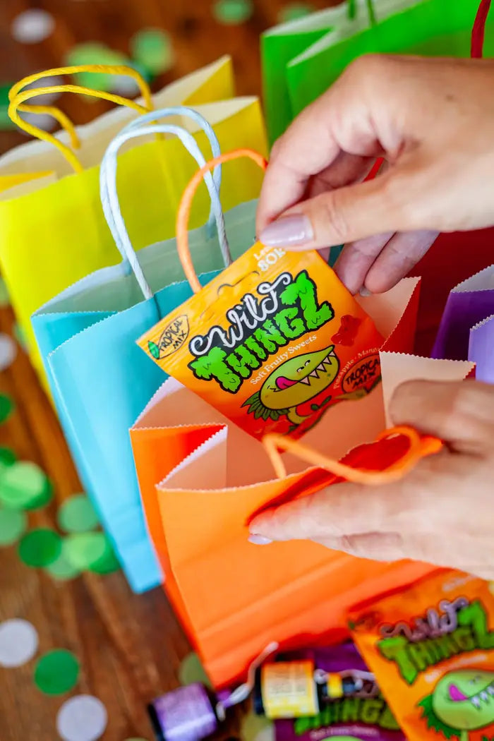Hands filling colourful party bags with bags of Tropical Mix