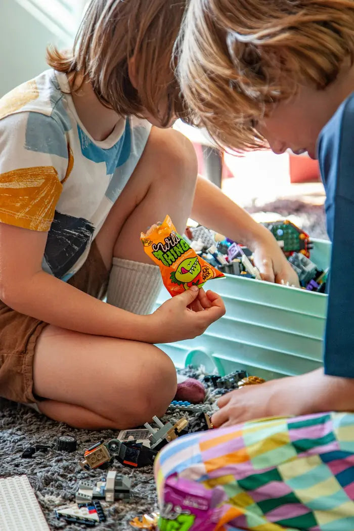 Two children playing with Lego, one holding a bag of Tropical Mix